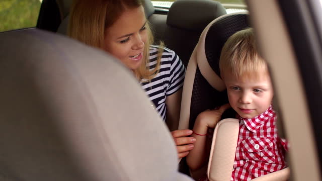 A-little-boy-sitting-in-a-car-seat,-sitting-next-to-his-mother.