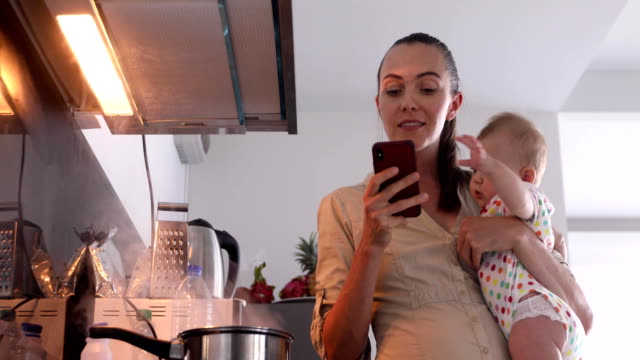 Mujer-sostiene-el-bebé-sus-brazos-al-mismo-tiempo-mira-en-el-teléfono