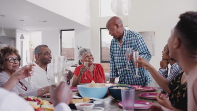 Großvater-steht-am-Esstisch-und-schlägt-einen-Toast-während-einer-Familienfeier-vor