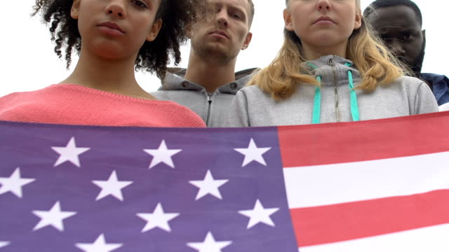 Young-people-silently-holding-American-flag-honoring-shooting-victims,-mourn