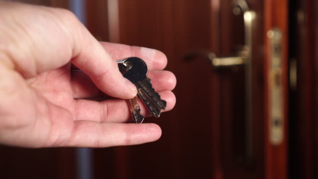 Shiny-new-keys-to-the-apartment-in-the-man’s-hand-and-ajar-brown-lacquered-lacquered-door-with-a-handle-and-a-lock-of-bronze-color