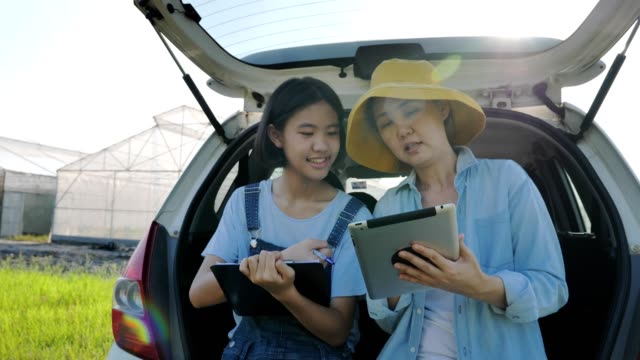 Familia-asiática-inteligente-sentada-en-el-coche-y-el-uso-de-la-tableta-digital-para-el-acceso-a-Internet-frente-a-la-casa-verde,-concepto-de-agricultura-inteligente