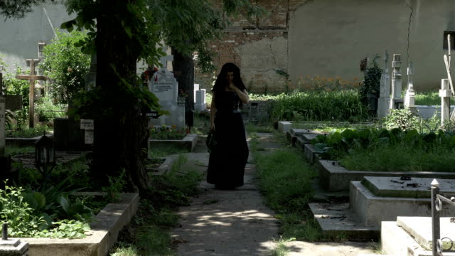 Grieved-widow-filled-with-sorrow-leaving-from-departed-husband-grave-walking-in-cemetery-alley
