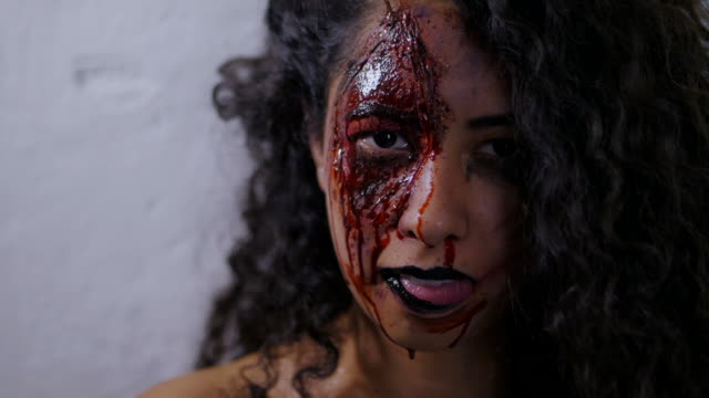 Scary-portrait-of-young-girl-with-Halloween-blood-makeup.-Beautiful-latin-woman-with-curly-hair-looking-into-camera-in-studio.-Living-dead-greasepaint.-Slow-motion