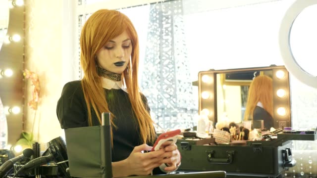 Junge-schöne-Mädchen-mit-Halloween-Make-up-mit-Smartphone-im-Schönheitssalon