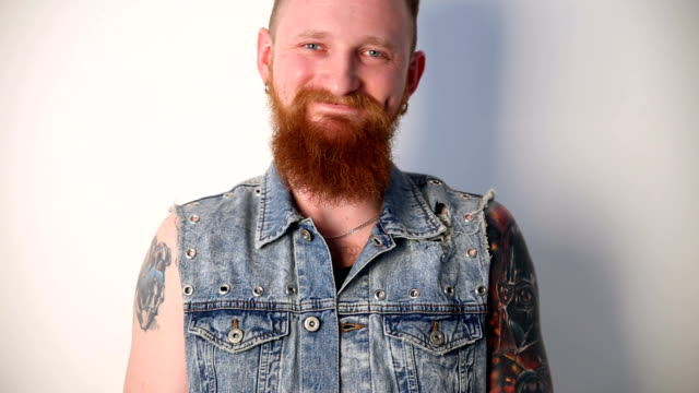 moderne-Jugend.-ein-fröhlich-Porträt-von-freundlich-lächelnden-Biker-mit-Tattoos-und-eine-stilvolle-Bart-und-Schnurrbart-in-eine-Jeansweste.