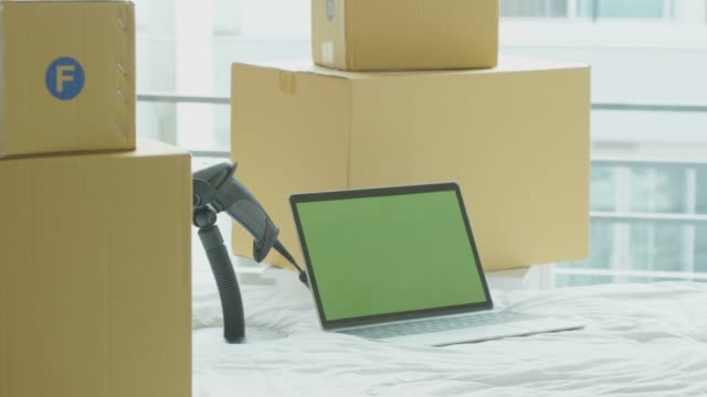 Dolly-shot:-laptop-computer-with-green-screen-chroma-key-on-the-bed-with-cardboard-boxes-around,-Online-business-concept.