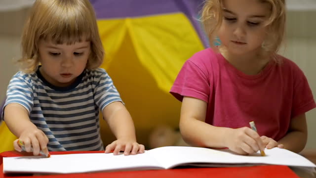 Zwei-kleine-Kinder-Mädchen-und-jungen-am-Tisch-zeichnen.-Bruder-und-Schwester-mit-bunter-Kreide-zeichnen