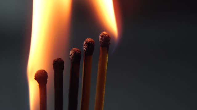 Brennende-Streichhölzer,-Kettenreaktion-und-Flamme.-Fünf-Matches-close-up-stehen-nebeneinander-auf-einem-schwarzen-Hintergrund