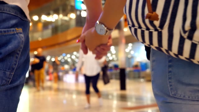 Young-couple-holding-hands-of-each-other-and-walking-at-terminal-of-airport.-Man-and-woman-taking-arms-and-stepping-during-trip.-Symbol-of-love-and-devotion.-Close-up-Rear-back-view