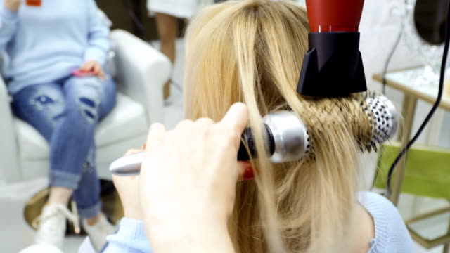 Friseur-trocknet-weibliche-Haare-mit-Fön-und-Bürste