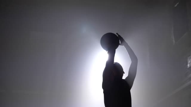 Silueta-de-jugador-de-baloncesto-tirar-bola-en-el-aro,-humo-por-todas-partes,-reflector-en-el-fondo