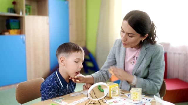 A-attractive-woman-speech-therapist-teaches-a-preschool-boy-at-a-speech-therapy-session