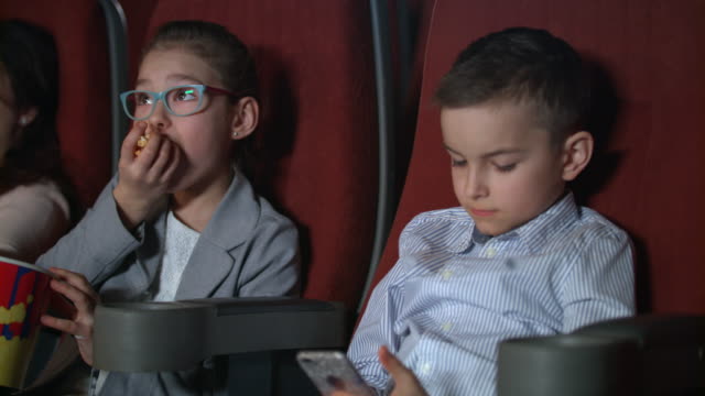 Kleine-Mädchen-essen-Popcorn-im-Kino.-Junge-mit-Smartphone-im-Kino