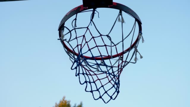 Lanzar-bola-en-el-aro-de-baloncesto-contra-el-cielo-azul,-a-través-de-aro,-al-aire-libre