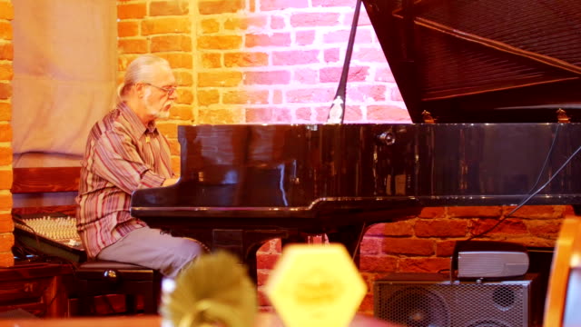 Hombre-de-pelo-gris-con-una-cola-en-la-cabeza-con-gafas-tocando-el-piano-en-un-bar-de-jazz