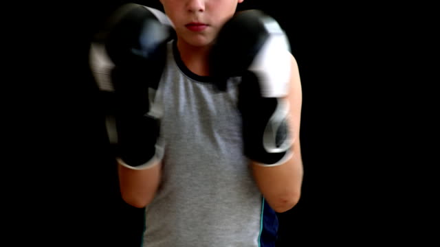 A-young-boxer-in-a-gray-sports-shirt-stands-on-a-dark-background,-he-holds-his-hands-in-gloves-on-the-body,-the-boy's-head-and-legs---off-screen