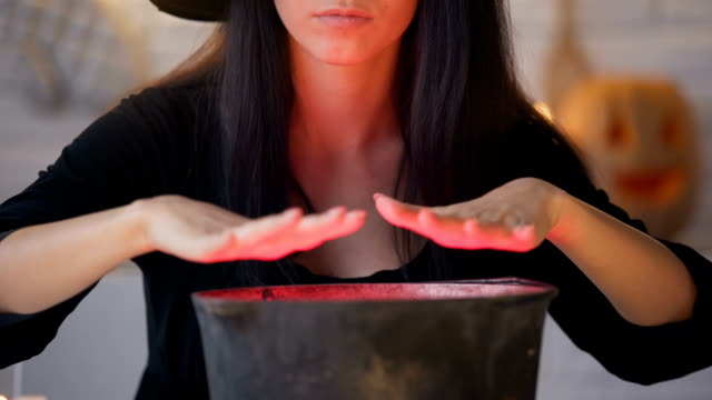 Young-witch-in-black-dress-conjuring-and-cooking-potion,-Halloween-eve-magic
