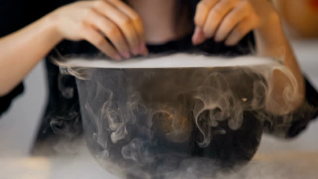 Woman-in-witch-costume-making-conjuring-gestures-above-magical-pot-with-potion