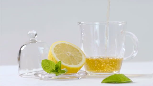 Herbal-tea-being-poured-into-transparent-teapot,-lemon-and-mint-leaves-around