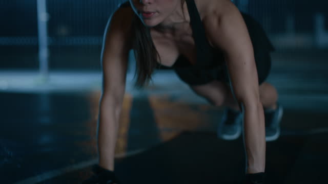 Exhausted-Beautiful-Sporty-Fitness-Girl-Doing-Push-Up-Exercises.-She-is-Doing-a-Workout-in-a-Fenced-Outdoor-Basketball-Court.-Night-Footage-After-Rain-in-a-Residential-Neighborhood-Area.