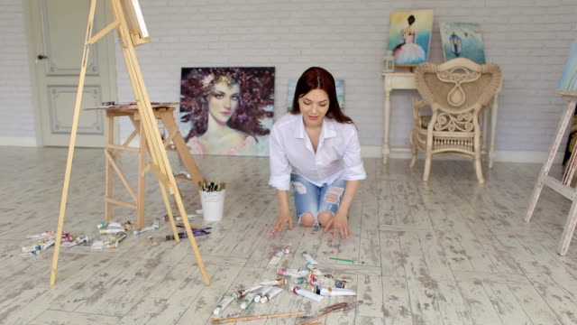 A-talented-girl-artist-throws-tubes-of-oil-paint-on-floor-in-Studio-for-drawing.