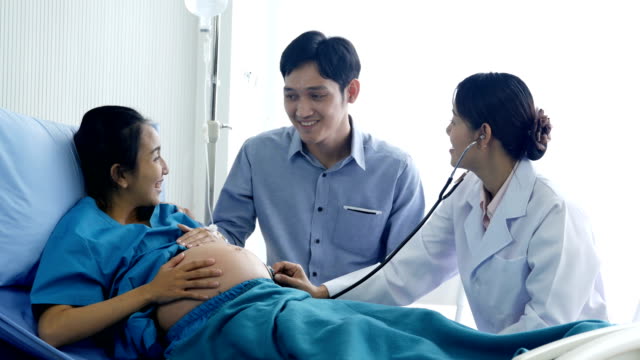 Female-doctor-visiting-to-pregnant-woman-at-hospital.-Pregnant-woman-and-he-husband-talking-to-doctor-with-happy-emotion.-People-with-healthcare-and-medical-concept.