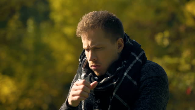 Sick-male-in-scarf-coughing-and-sneezing-in-autumn-park,-caught-cold,-infection