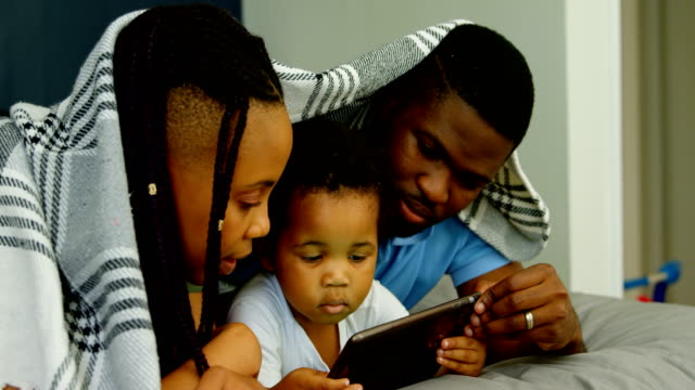 Seitenansicht-der-jungen-schwarzen-Familie-mit-digitalem-Tablet-auf-dem-Bett-im-Schlafzimmer-des-komfortablen-Hauses-4k