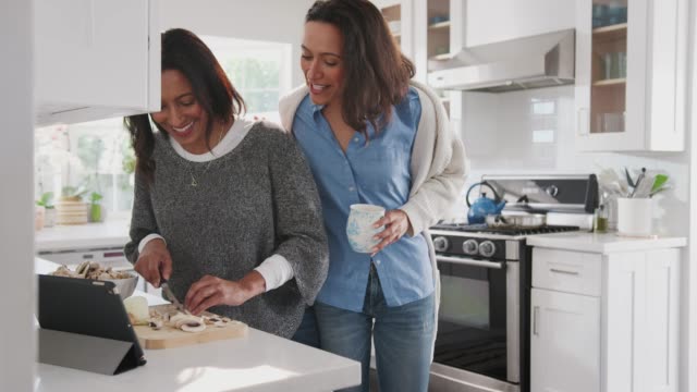 Middle-aged-woman-preparing-food-in-the-kitchen,-her-adult-daughter-standing-with-her-talking