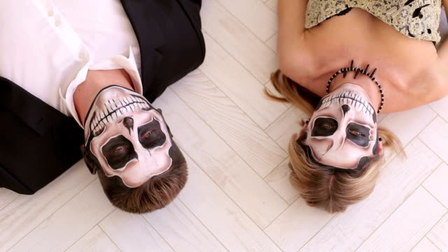 A-couple-in-carnival-costumes-lie-on-the-floor-on-a-white-floor.-Halloween-party