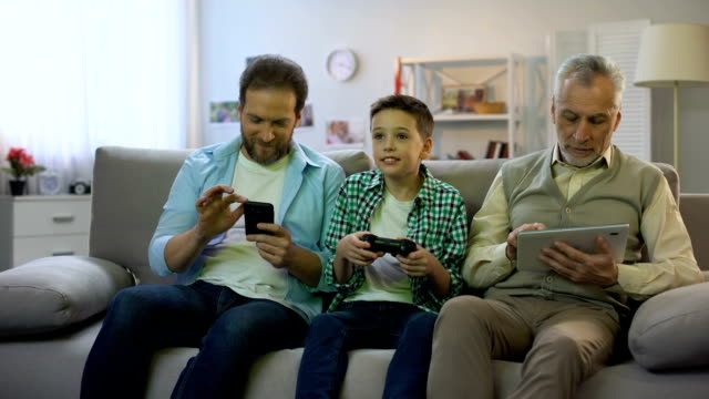 Adult-males-scrolling-gadgets,-preteen-boy-playing-video-game,-gadget-addiction
