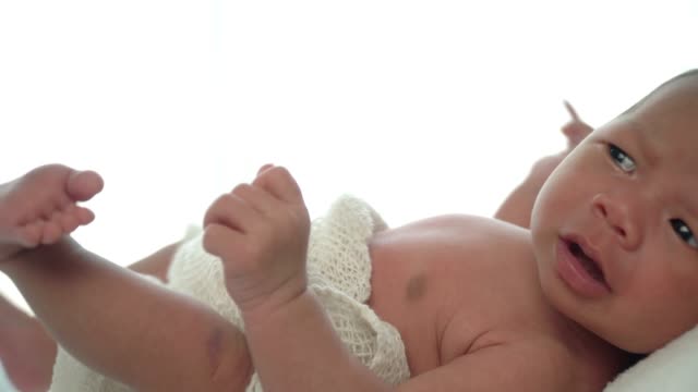 4K-Video-Selective-focus-real-time-dolly-shot-of-newborn-baby-girl-laying-down-on-white-bed-and-crying