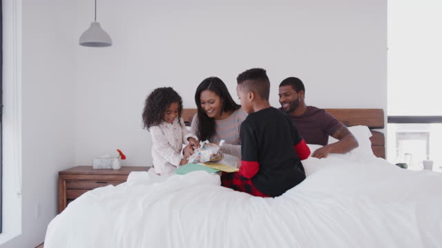 Children-Sitting-On-Parents-Bed-With-Gift-And-Card-To-Celebrate-Mothers-Day-Or-Birthday
