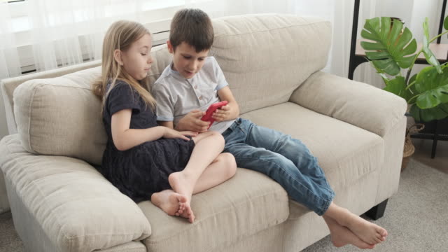 Girl-with-her-brother-playing-game-using-mobile-phone-on-sofa