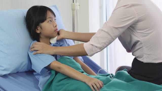 Asian-mother-rub-the-body-patient-little-girl-for-reduce-the-temperature-and-physical-examination-at-hospital.-Concept-of-family,-medical,-healthcare-and-technology.