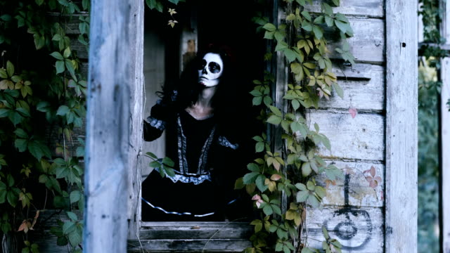 Eine-junge-Frau-mit-gruseligem-Skelett-Halloween-Make-up-blick-aus-dem-Fenster.-4K