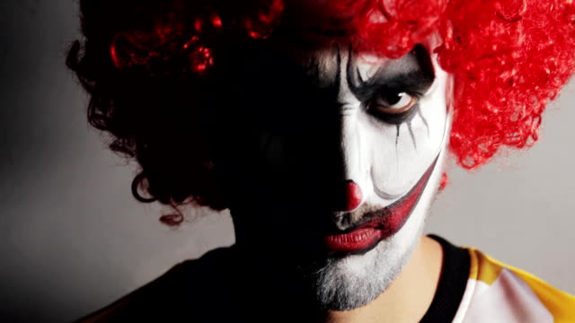 Böse-wütende-Gesicht-mit-Makup-von-beängstigend-Clown-schaut-in-die-Kamera-in-dunkel-auf-Halloween