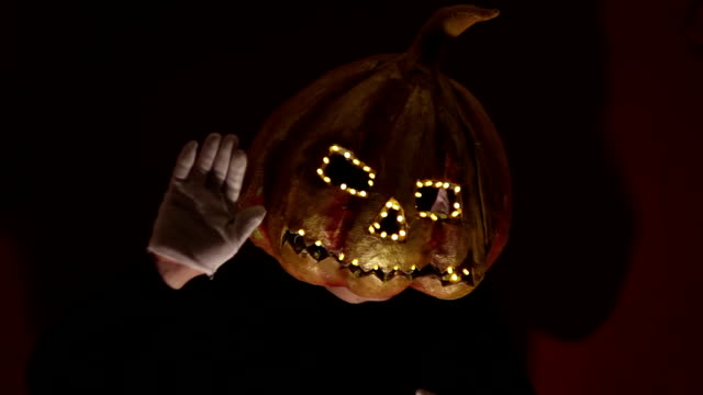 Scary-man-with-a-pumpkin-head-and-luminous-eyes-looks-at-the-camera.-Man-with-a-pumpkin-head-scares-raising-his-hands-up.-Halloween.
