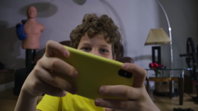 Face-of-cute-Caucasian-boy-with-tired-eyes-getting-angry-as-loosing-in-video-game.-Curly-haired-teenager-in-yellow-T-shirt-using-smartphone-to-play.-Gaming,-technologies.-Cinema-4k-ProRes-HQ.