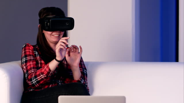 Muchacha-que-ríe-sentado-en-el-sofá-y-usando-laptop-mediante-gafas-de-realidad-virtual