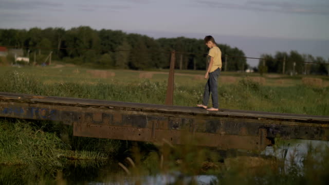 Frustrated-offended-lonely-boy-walks-along-a-bridge-near-a-river-in-countryside,-depressed-and-human-problems