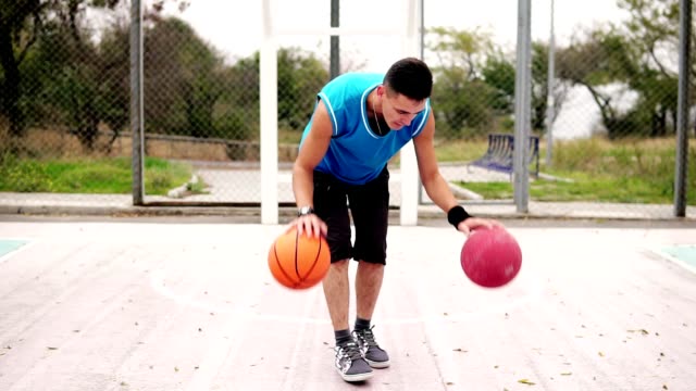 Vista-de-cerca-de-un-joven-practicando-baloncesto-en-la-cancha-de-calle.-Él-está-jugando-con-dos-bolas-simultáneamente.-Tiro-de-cámara-lenta