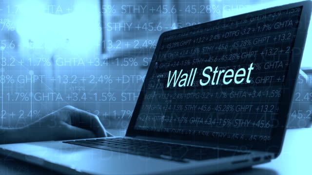 Laptop-with-stock-market-ticker-scrolling-in-background-with-test-on-screen---Wall-Street