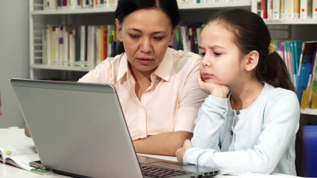 Mature-Asian-woman-helping-her-tired-daughter-with-homework