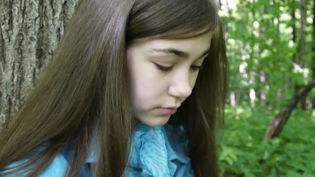 Retrato-de-linda-chica-adolescente-leyendo-el-libro-y-la-página-de-inflexión-apoyado-contra-el-tronco-de-árbol-en-el-bosque-en-primavera,-estudiar-al-aire-libre