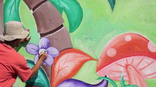 Mural-painter-paints-a-flower-image-in-color-on-the-school-wall.-time-lapse