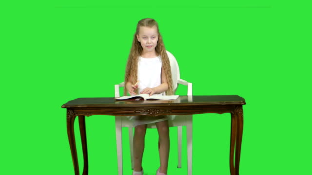 Cute-little-girl-doing-homework,-writing-down-on-a-Green-Screen,-Chroma-Key