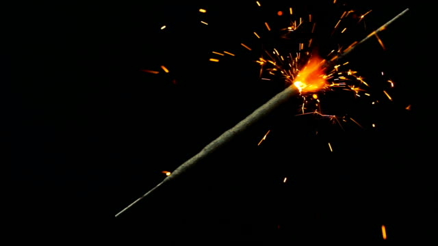 Bengal-lights.-One-stick-of-Bengal-fire-located-on-a-diagonal-of-a-frame,-lights-up-an-orange-glow.-Sparks-fly-apart-in-different-directions.-Shooted-on-a-black-background,-can-be-used-in-your-video-as-an-element.