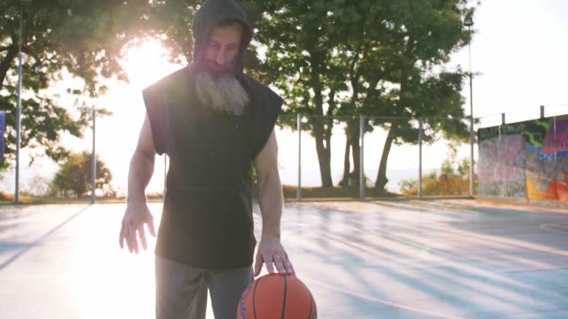 Stylish-middle-aged-man-with-long-gray-bearded-playing-basketball-during-sunset